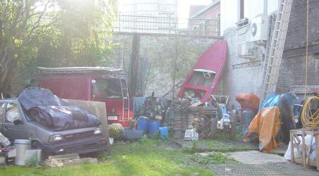 Photo d'un terrain vague tout près de la Place du Jeu de Balle (quartier des Marolles - Bruxelles Centre): on y trouve les carcasse d'une voiture et d'une camionnette, un hors-bord, des bidons, du matériel divers tant bien que mal recouvert de bâches…