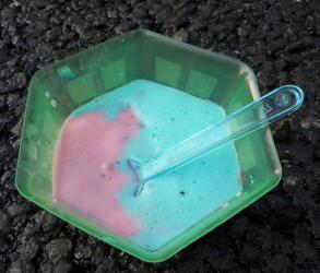 Photo d'un ravier de glace fondue (bleu clair et rose) déposé sur un macadam tout neuf