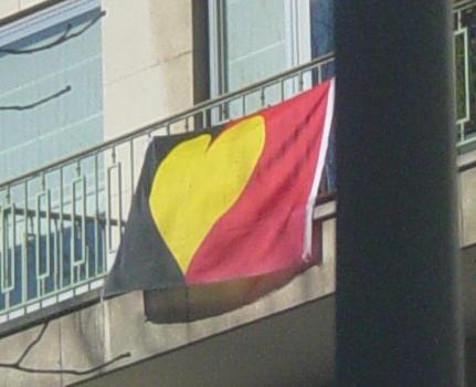 Photo d'un drapeau belge dont la bande centrale jaune est remplacée par un cœur jaune