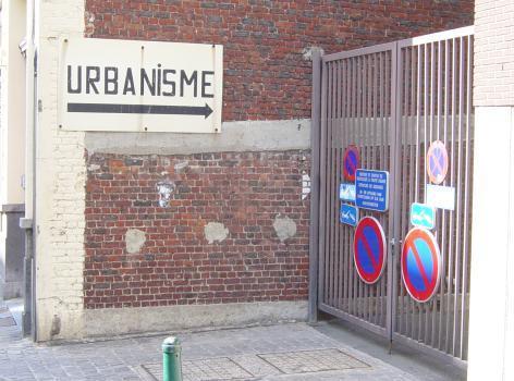 Sur un vieux mur rafistolé figure le panneau «urbanisme» souligné d'une flèche renvoyant vers une grille fermée, sur laquelle figurent quatre panneaux d'interdiction de stationner et trois panneau montrant une dépanneuse enlevant une voiture. Bref, rien de très engageant.